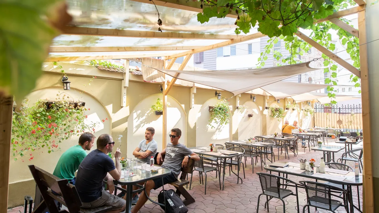 Terasa restaurantului Bucătărașul cel Dibaci, cu mese sub pergolă și plante verzi